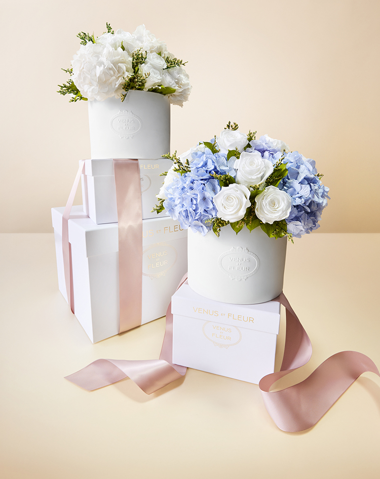 White and blue floral arrangements in white boxes with pink ribbons.