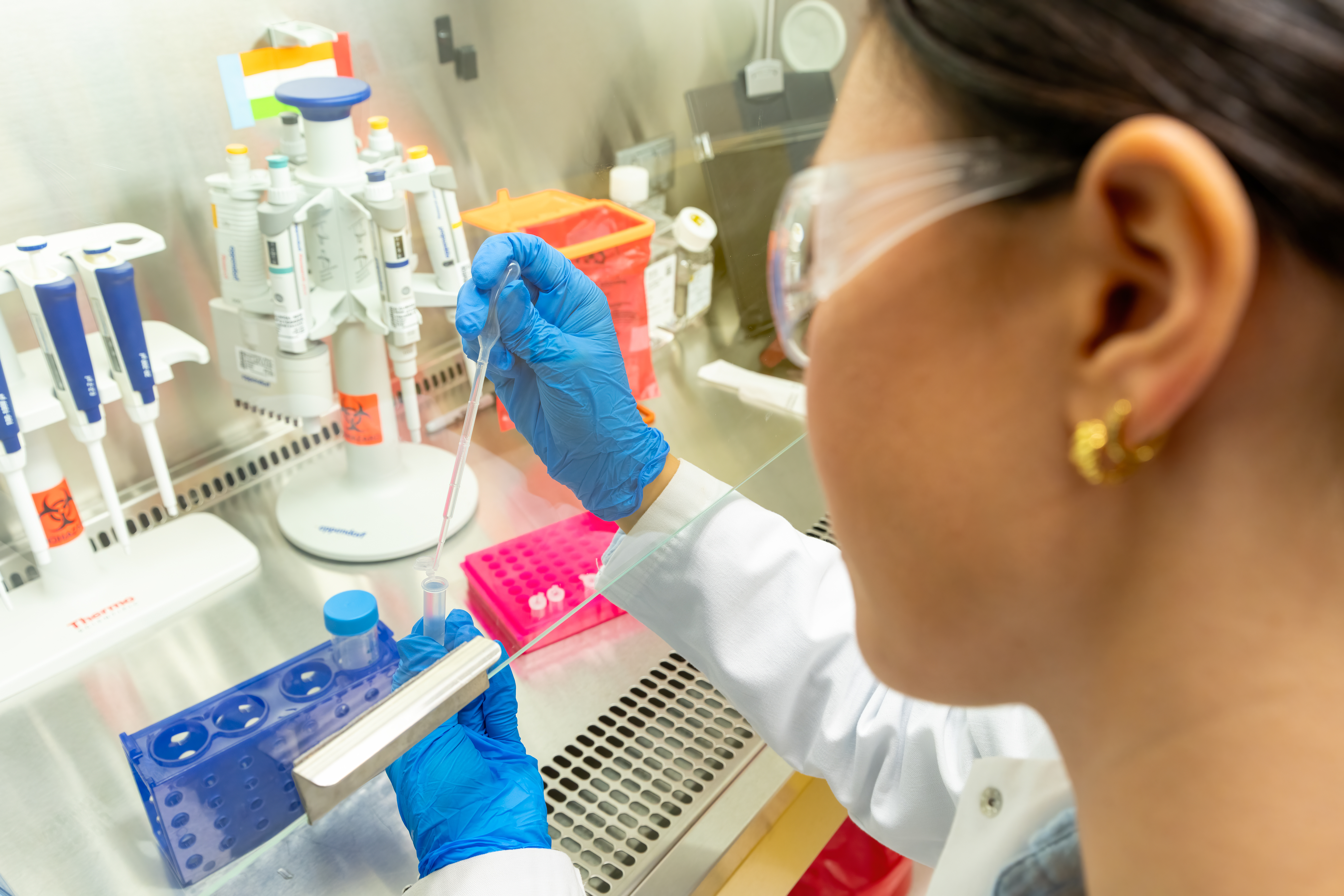 Person in lab coat and gloves using pipette in laboratory.