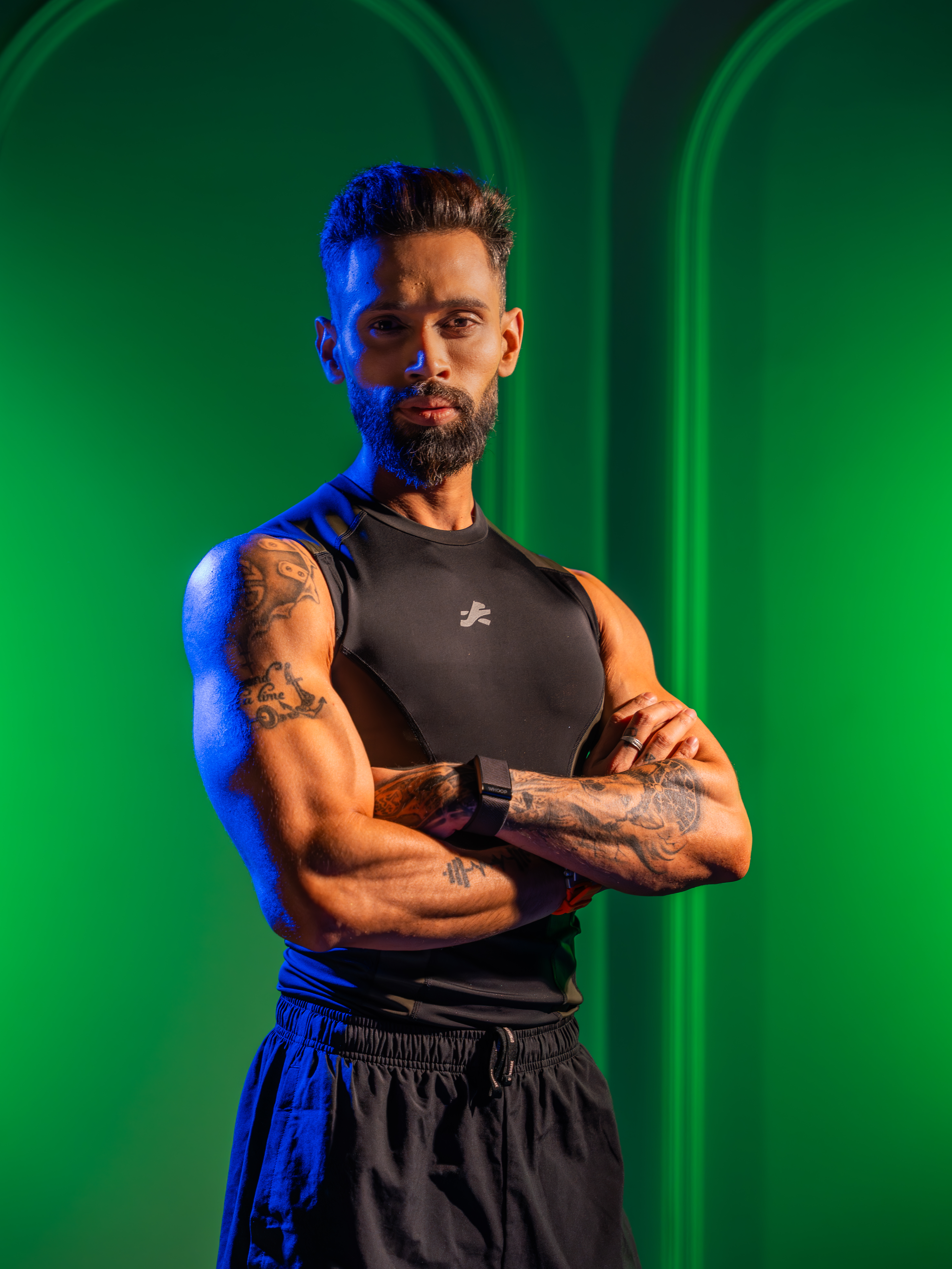 Man with tattoos in athletic wear against a green background.