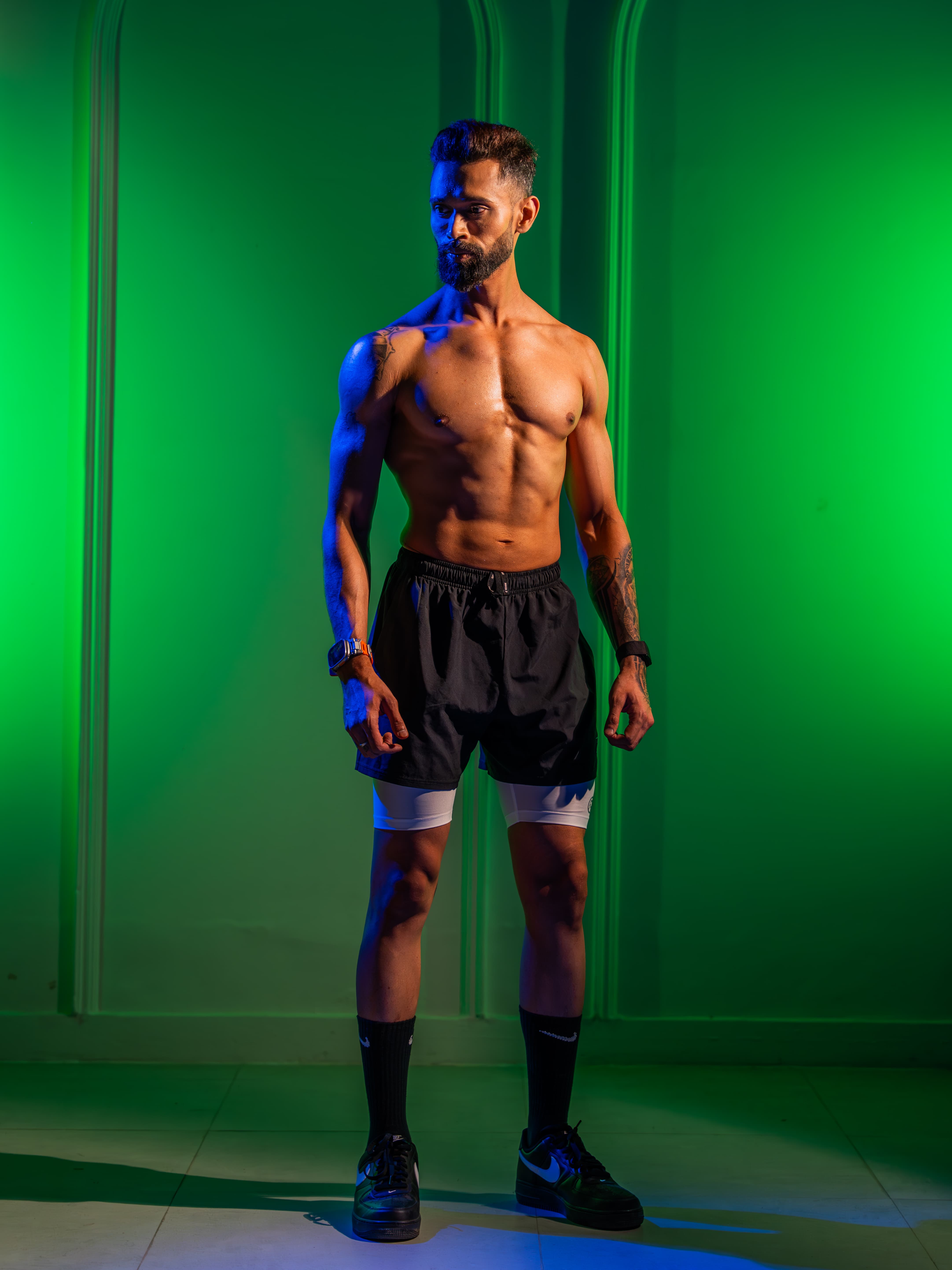 Man in athletic shorts standing against a green background, lit with blue and green lights.