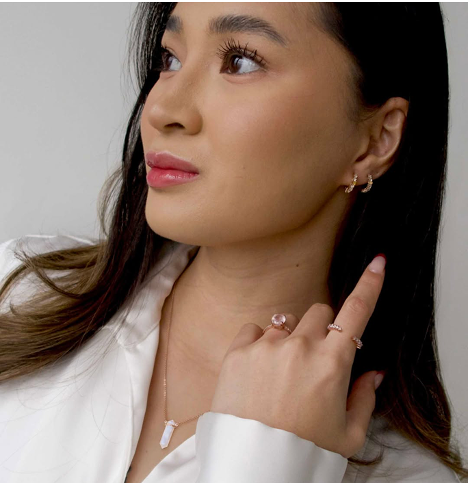 Woman wearing earrings, rings, and a necklace, looking to the side.