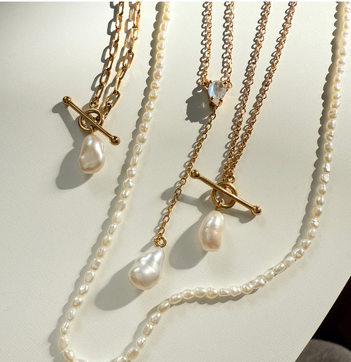 Gold and pearl necklaces with toggle clasps on a light background.