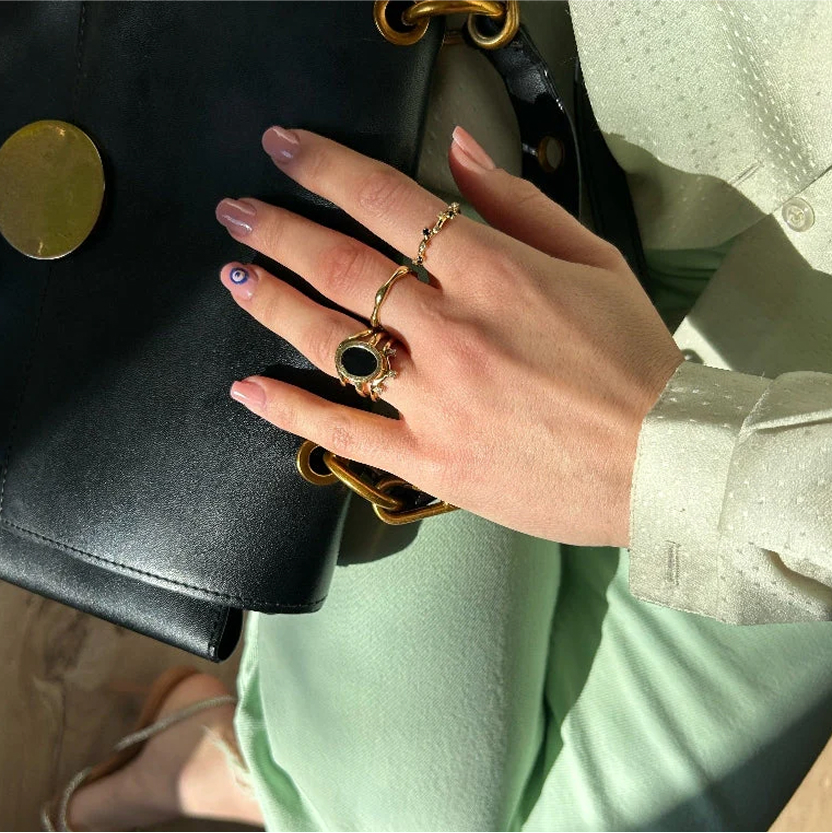 Hand with rings holding a black handbag with gold chain.