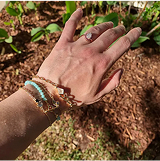 A hand with bracelets and a ring, outdoors near plants.