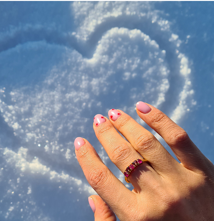 Hand with pink nails and ring over heart shape in snow.