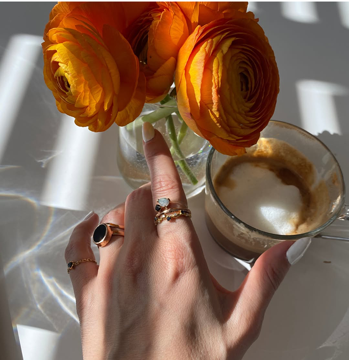 Hand with rings near orange flowers and a cup of coffee.