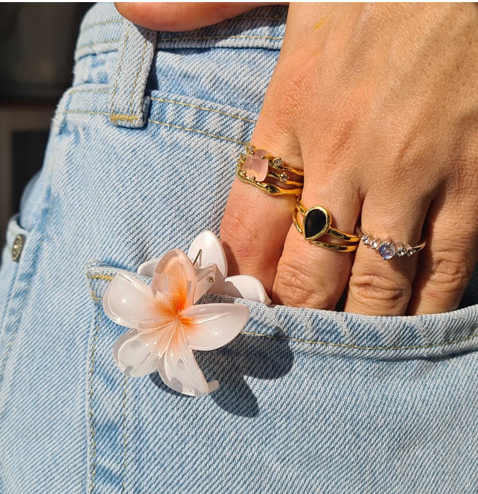 Hand with rings holding a flower clip in a denim pocket.