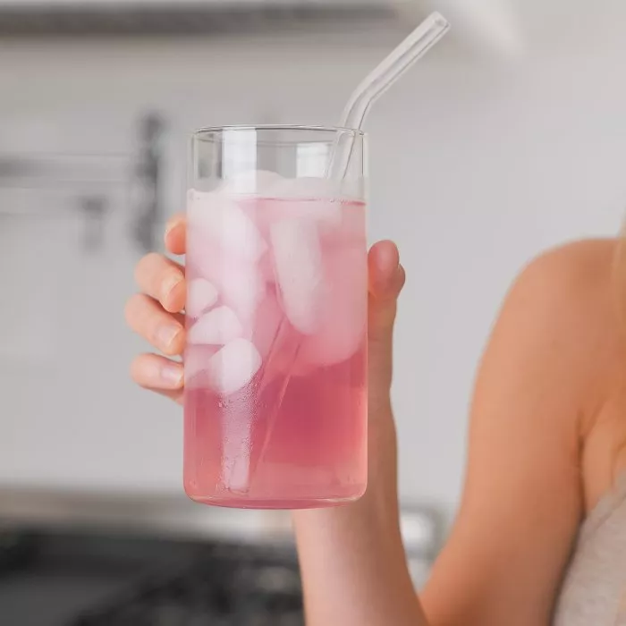 Hand holding a glass of pink iced drink with a straw.