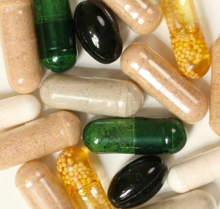 A close-up overhead view of various supplement capsules in different colors and textures on a white surface.