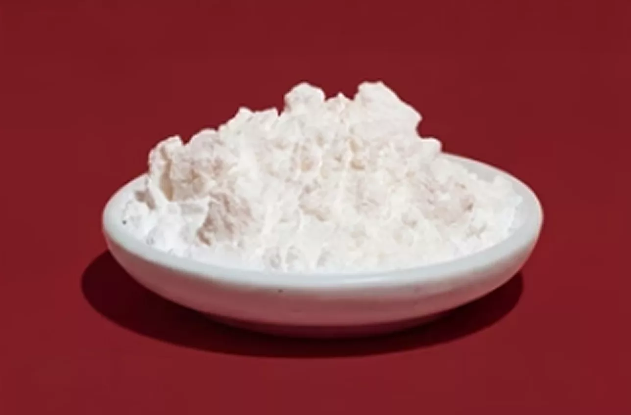 A small white bowl of lumpy white powder sits on a red background.