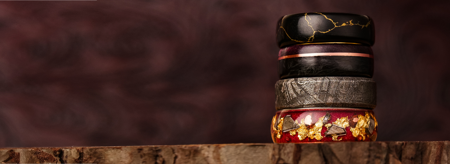 A close-up of a stack of five uniquely designed rings resting on a rustic wooden surface.