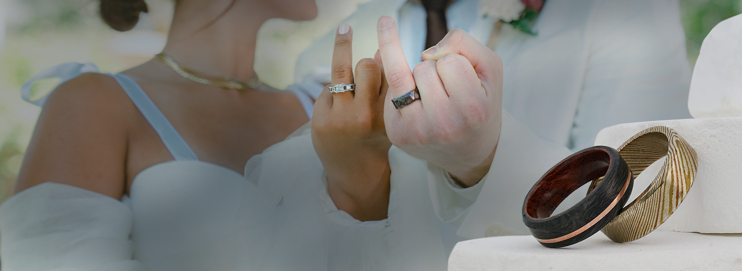 A married couple links pinky fingers to show their wedding rings, with other rings in the foreground.