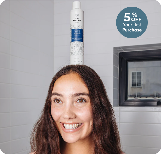 Smiling woman balancing a shampoo bottle on her head in a bathroom.