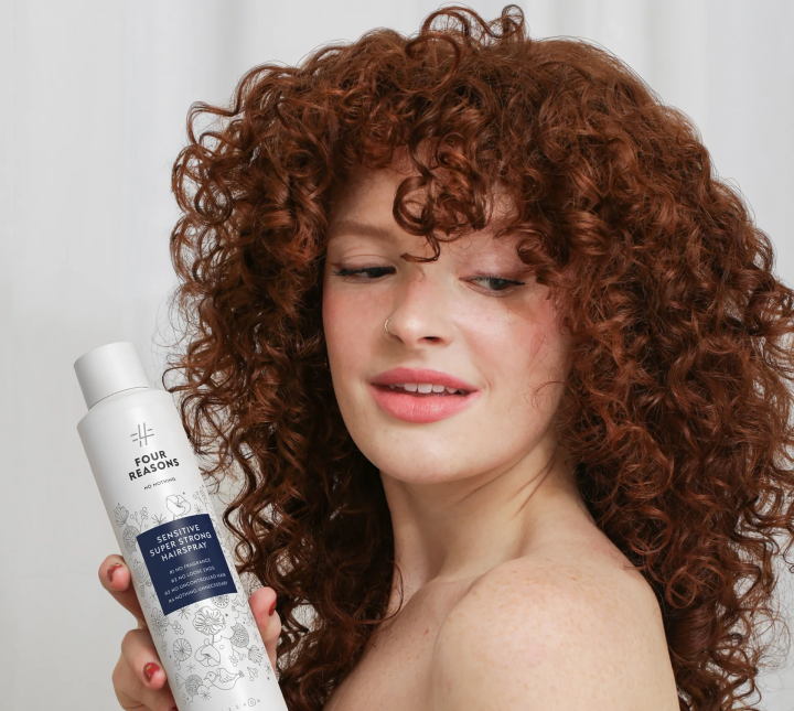 Person with curly hair holding a bottle of hairspray.