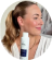 Person holding a skincare product, smiling, with hair tied back.