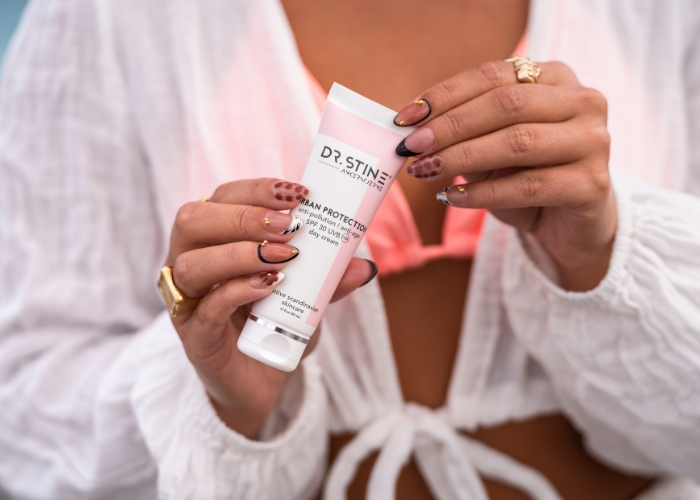 A woman with a decorative manicure holds a tube of Dr. Stine Urban Protection day cream.