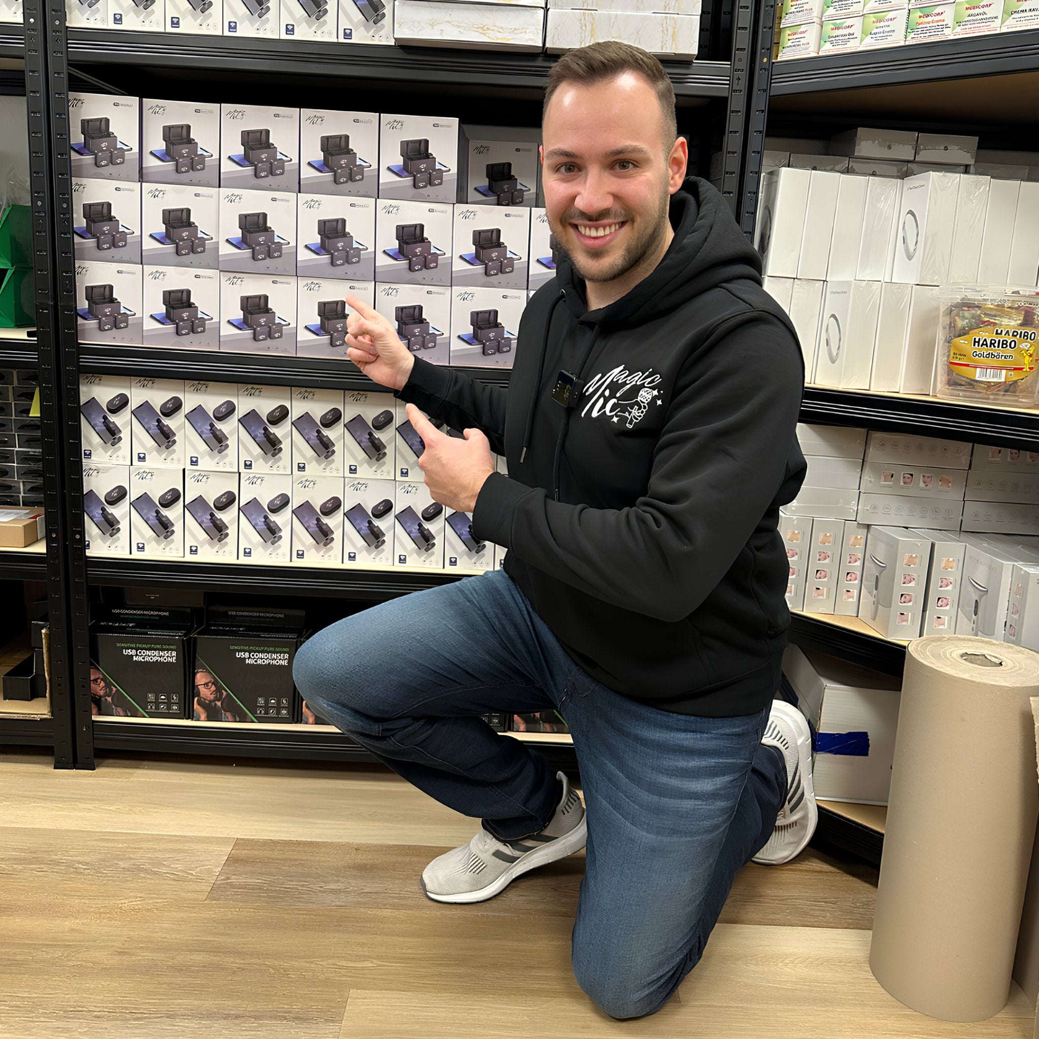 Person smiling and pointing at a shelf filled with electronic product boxes.