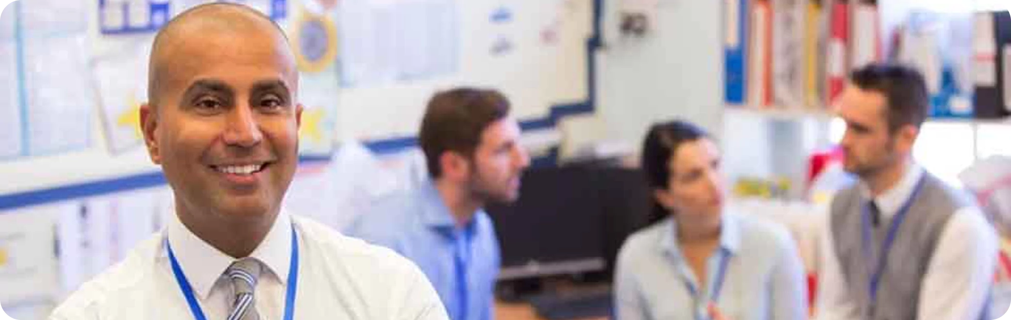 Smiling man in focus with three people blurred in the background.