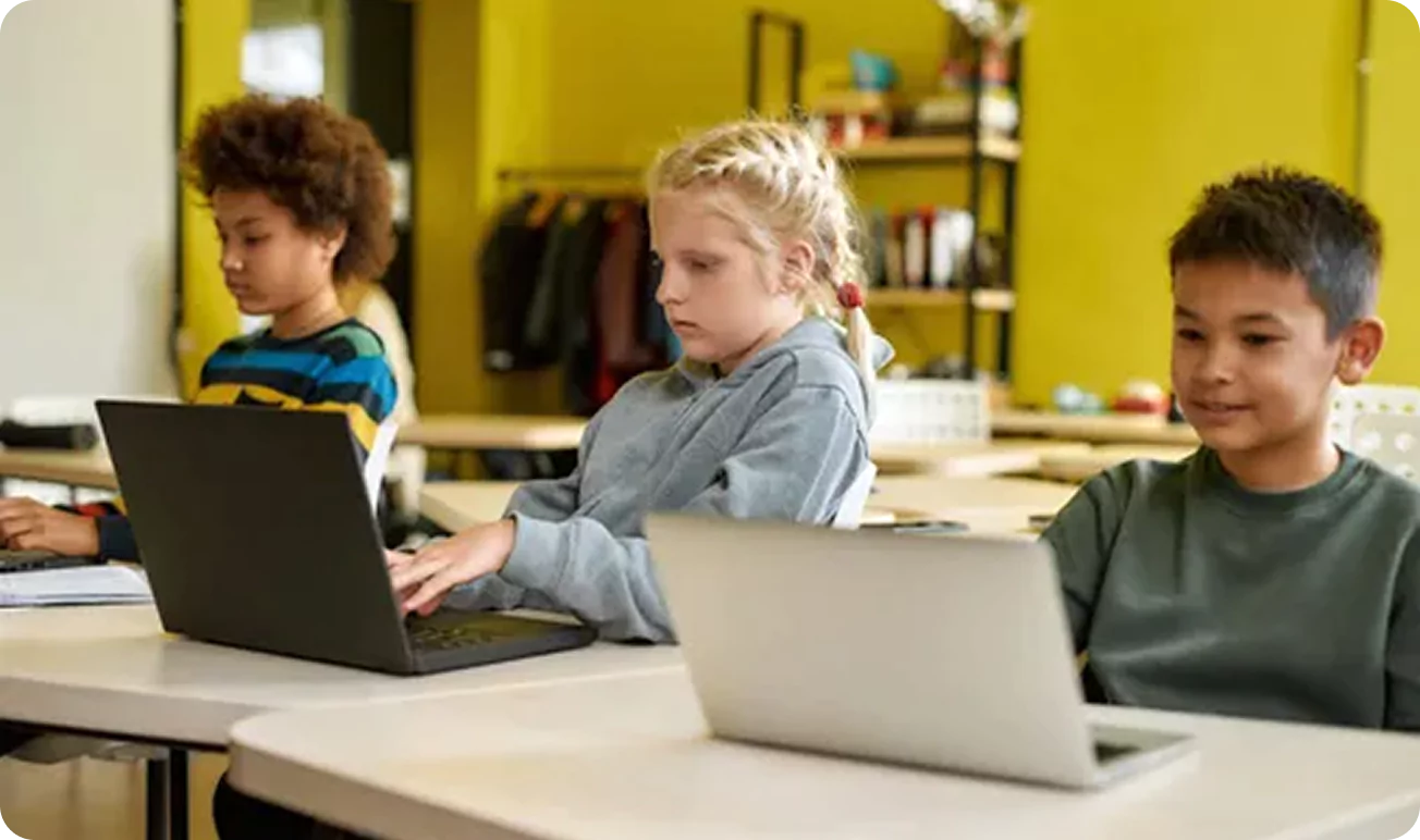 Three children using laptops in a classroom setting.