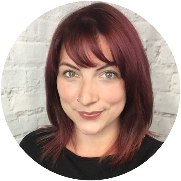 Person with red hair smiling against a white brick wall background.