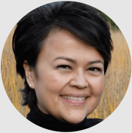 Smiling person with short dark hair in a field.