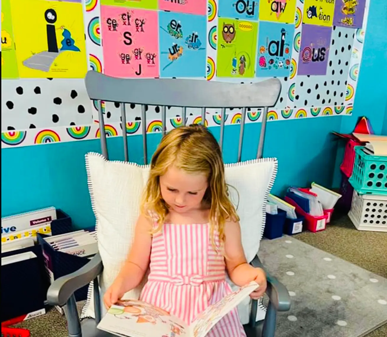 Child in a striped dress reading a book in a colorful classroom.