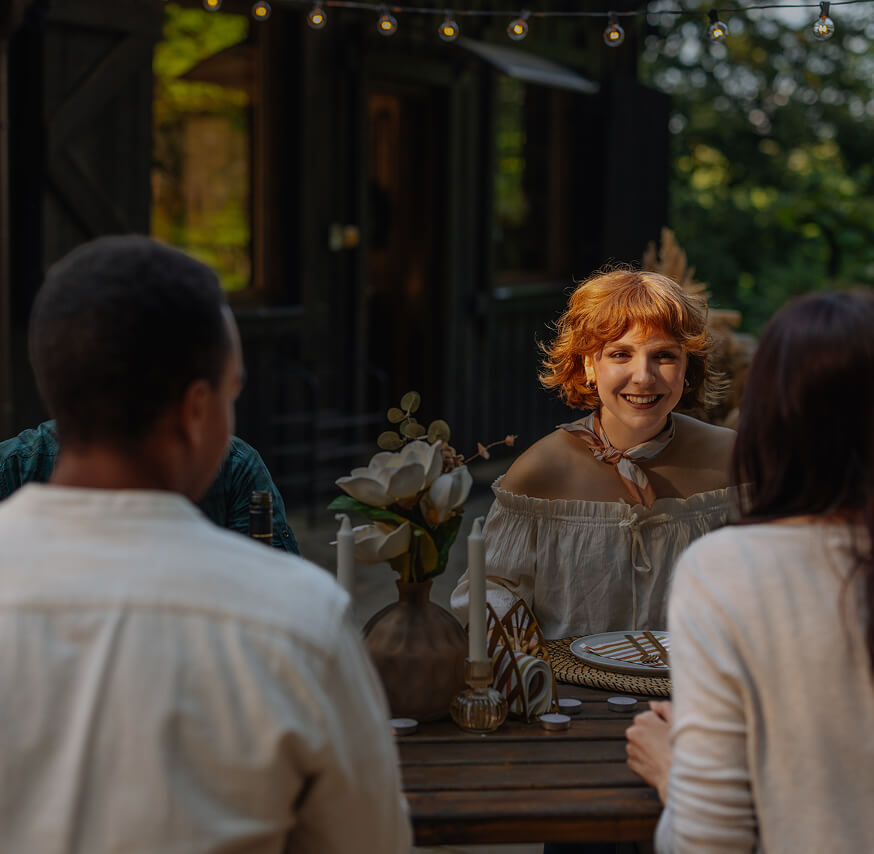 Group of people dining outdoors at a wooden table with candles and flowers.