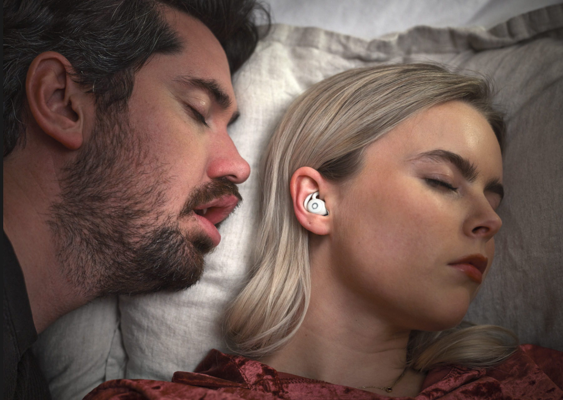 Two people sleeping, one wearing a white earbud.