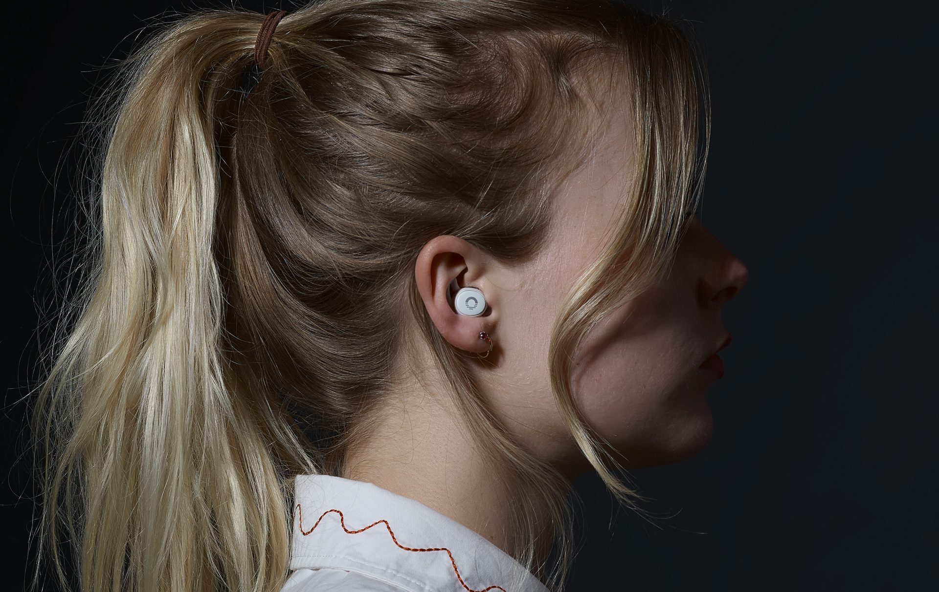 Side profile of a person wearing a white earbud.