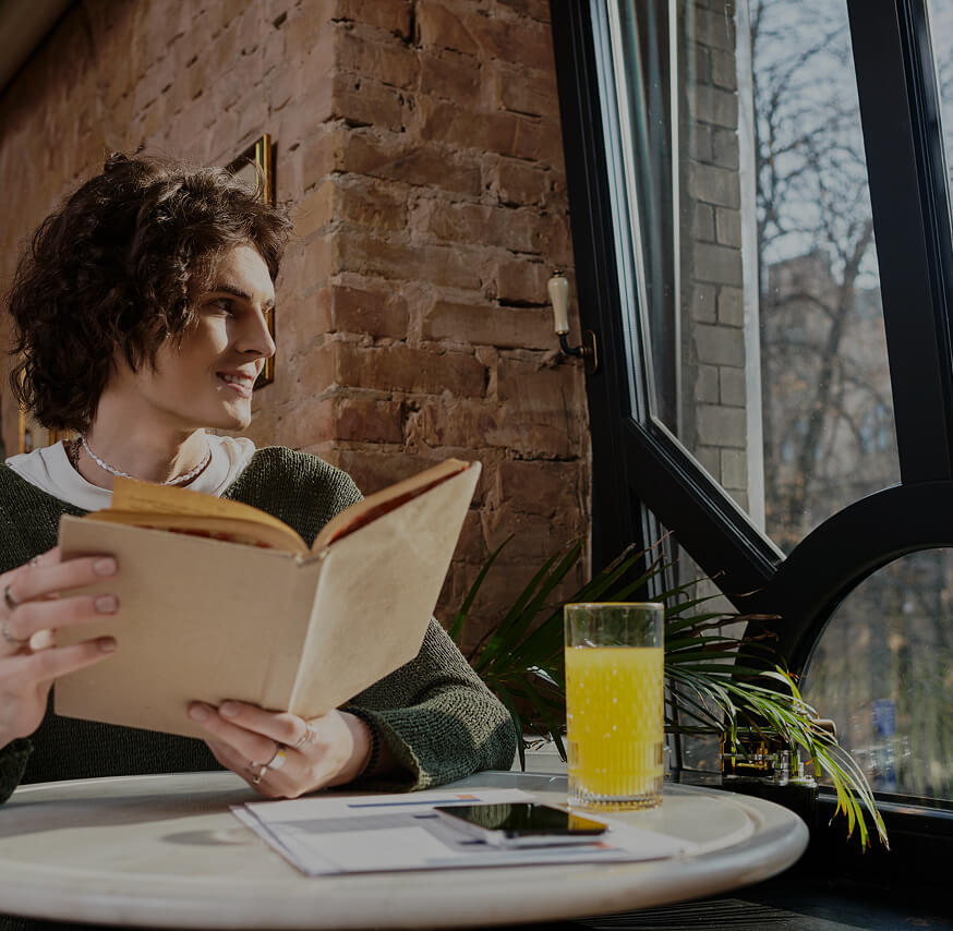 Person reading a book at a table with a drink and papers.