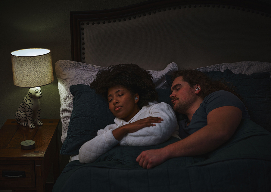 Two people sleeping in bed with earplugs, next to a lamp.