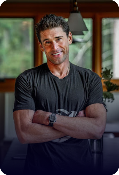 A smiling man in a black t-shirt with his arms crossed, standing indoors.