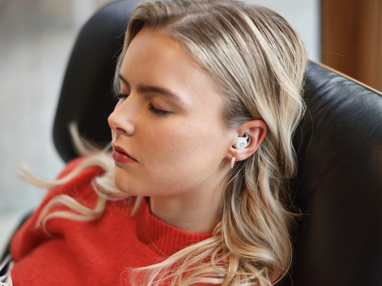 Person with closed eyes wearing earbuds, sitting on a black chair.