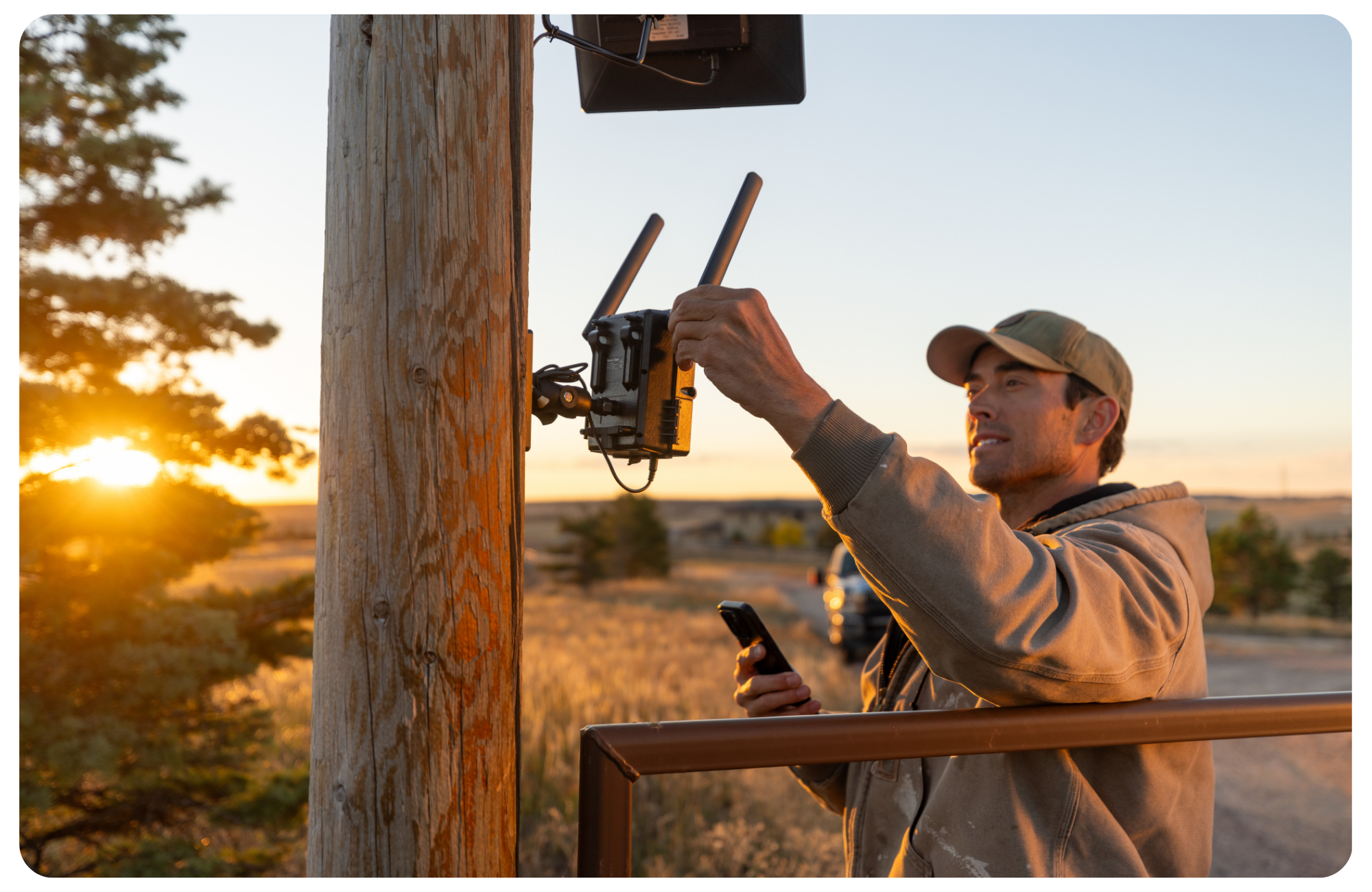 Person installing a device on a wooden pole at sunset.