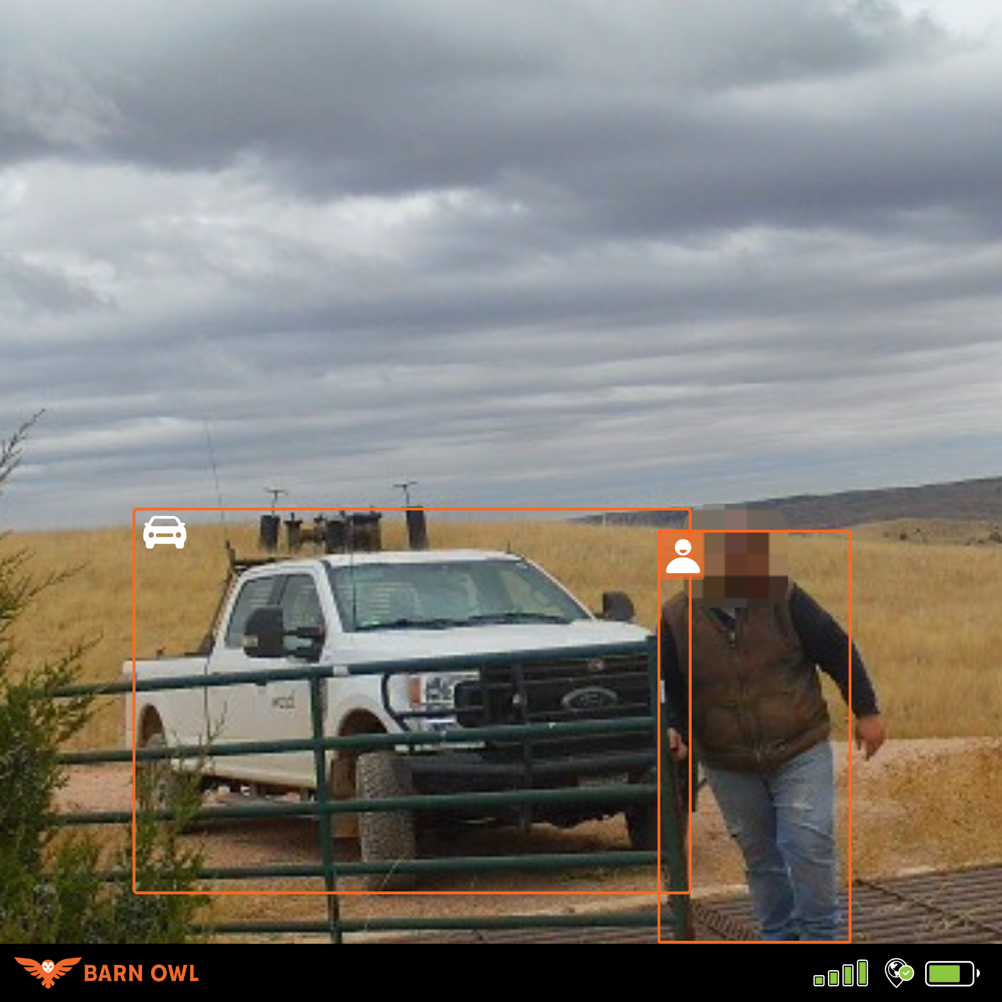White truck and person near a fence in a grassy field under cloudy sky.