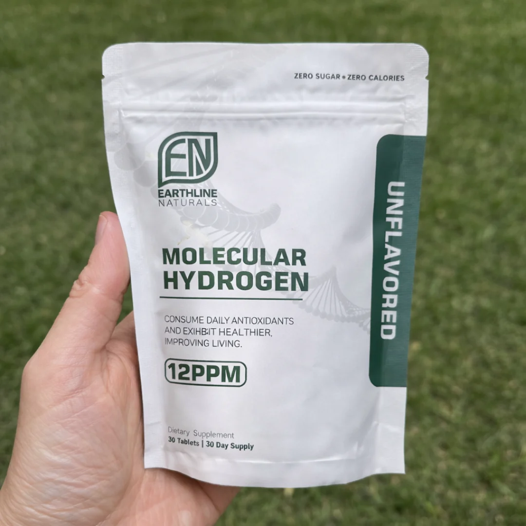 A hand holds a white pouch of Earthline Naturals Molecular Hydrogen dietary supplement against a grassy background.