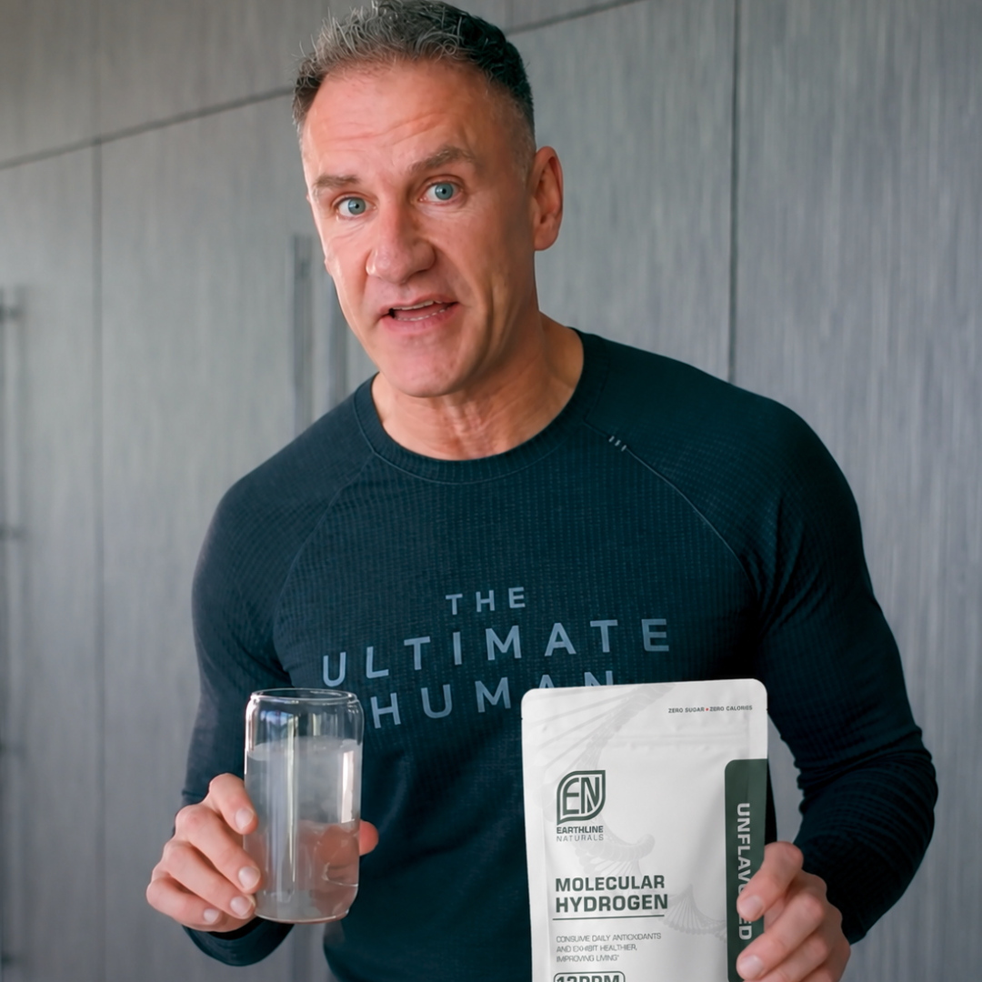 A man in a long-sleeved shirt holds a glass of water and a pouch of Molecular Hydrogen.