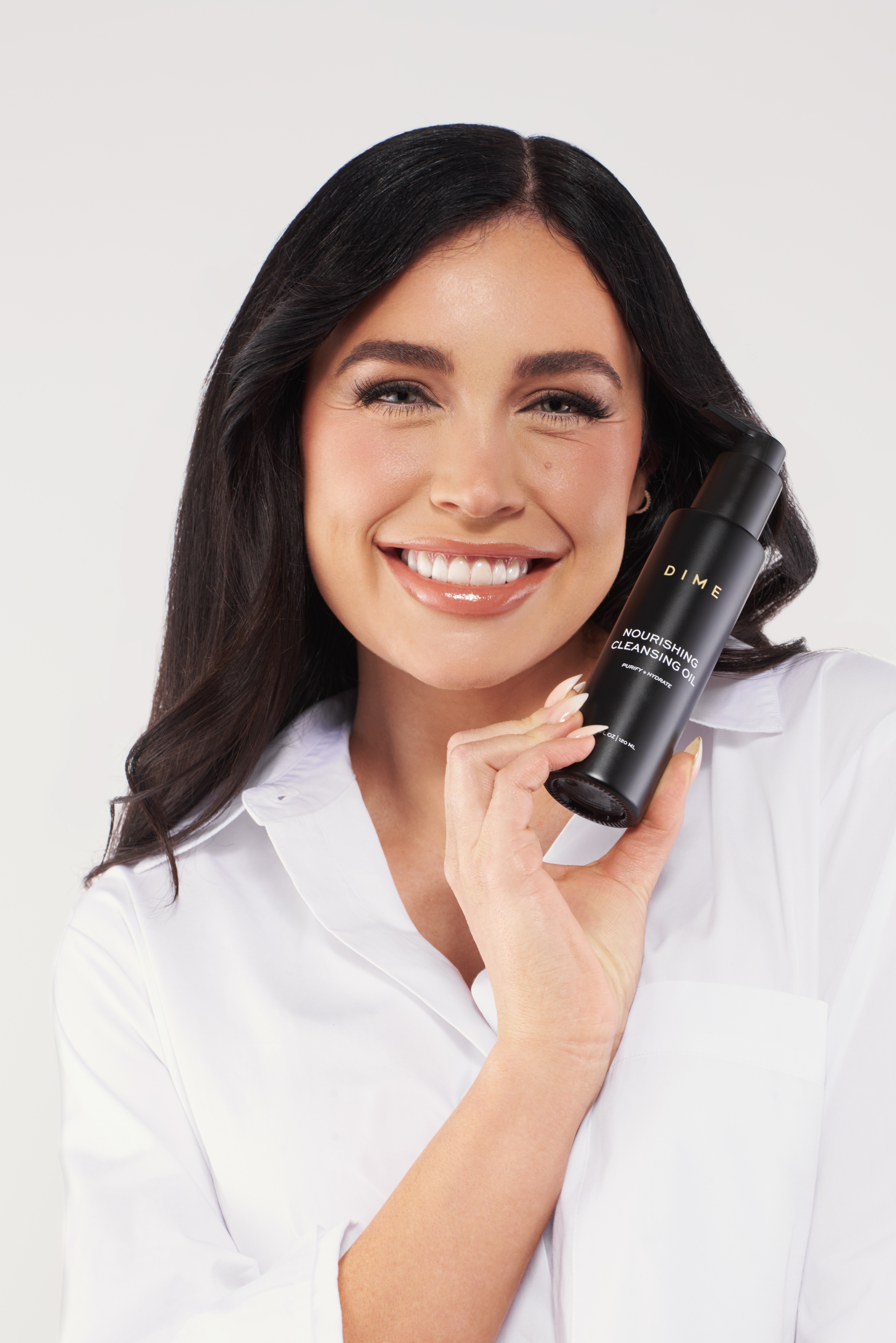 Person smiling, holding a bottle of DIME Nourishing Cleansing Oil.