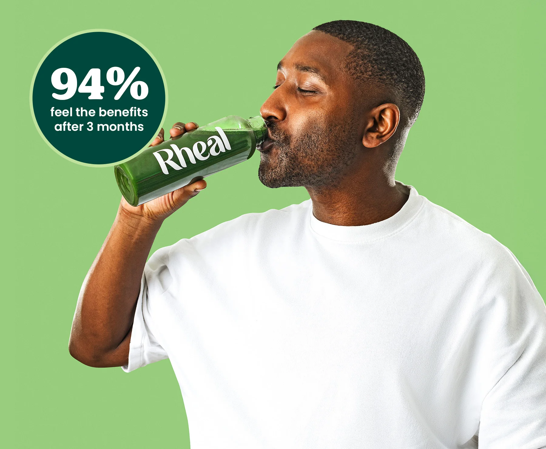 Person in white shirt drinking green beverage from a Rheal bottle.