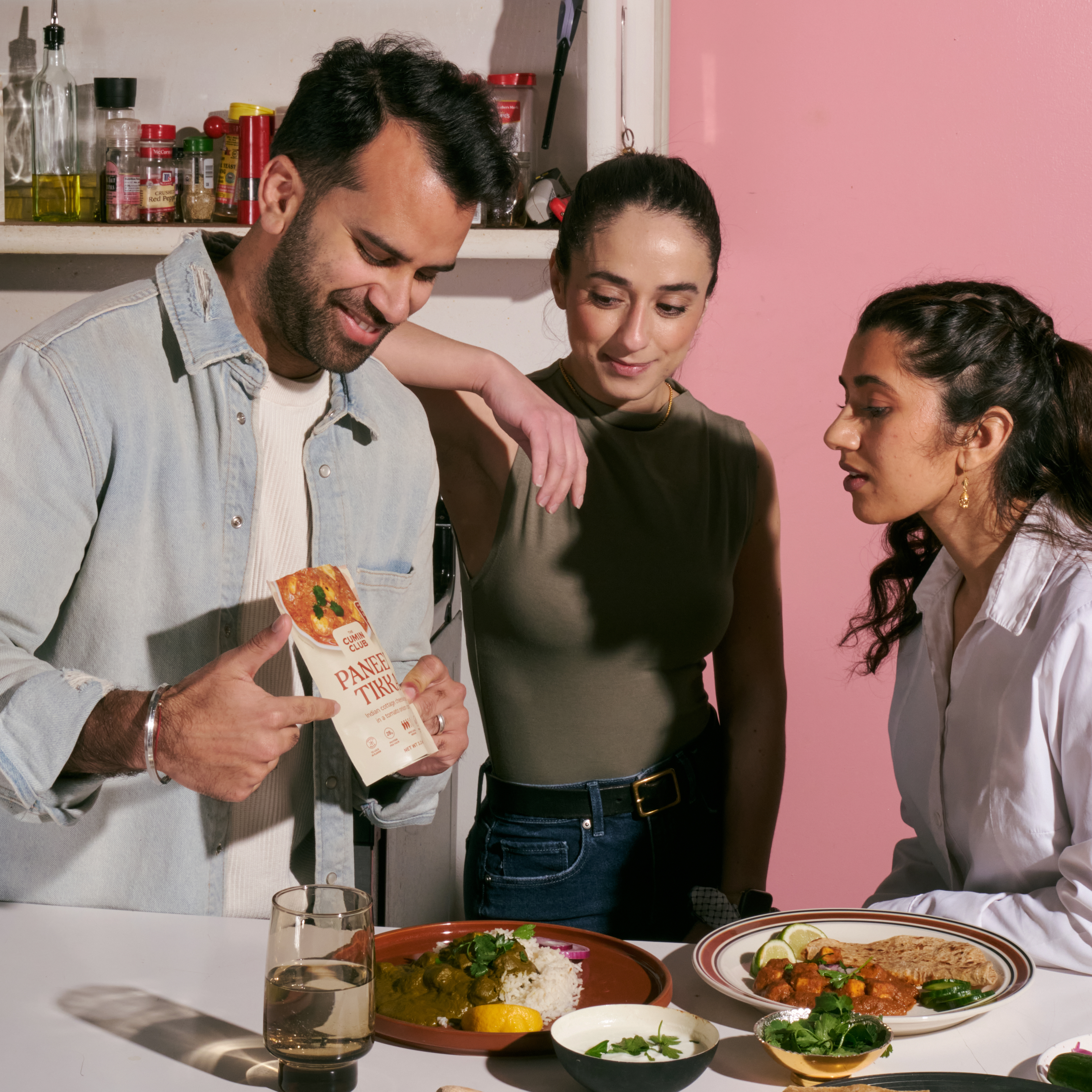 Three people in a kitchen with Indian food and a paneer tikka package.