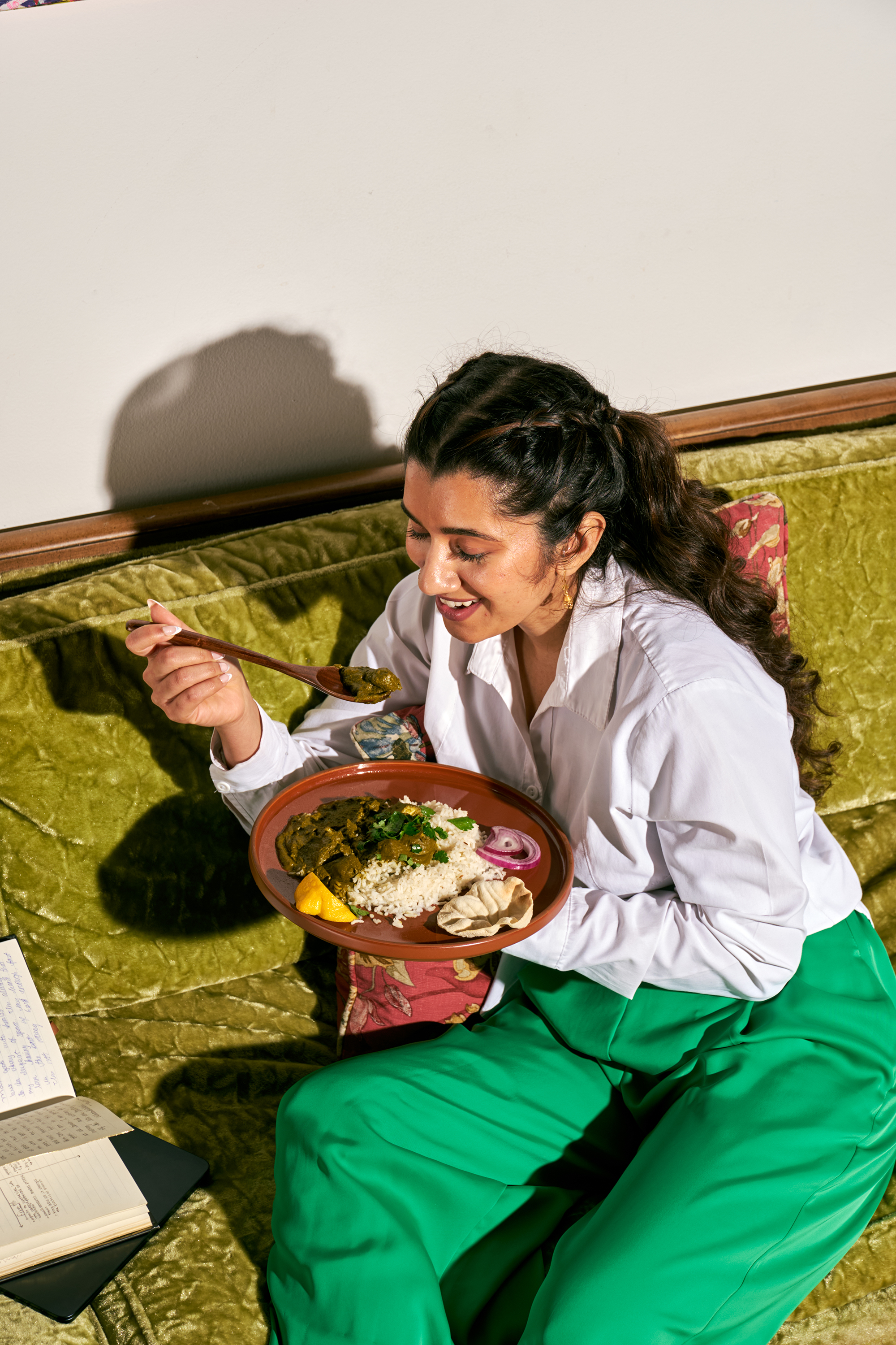 Person sitting on a couch eating a meal with rice and vegetables.