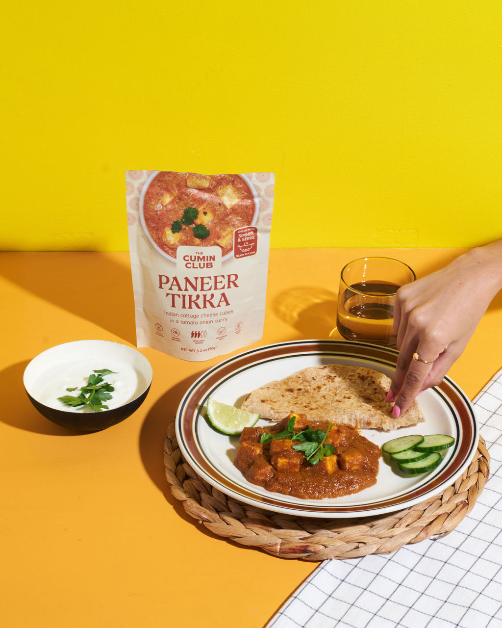 Plate of paneer tikka with roti, cucumber, lime, and a hand reaching for food.