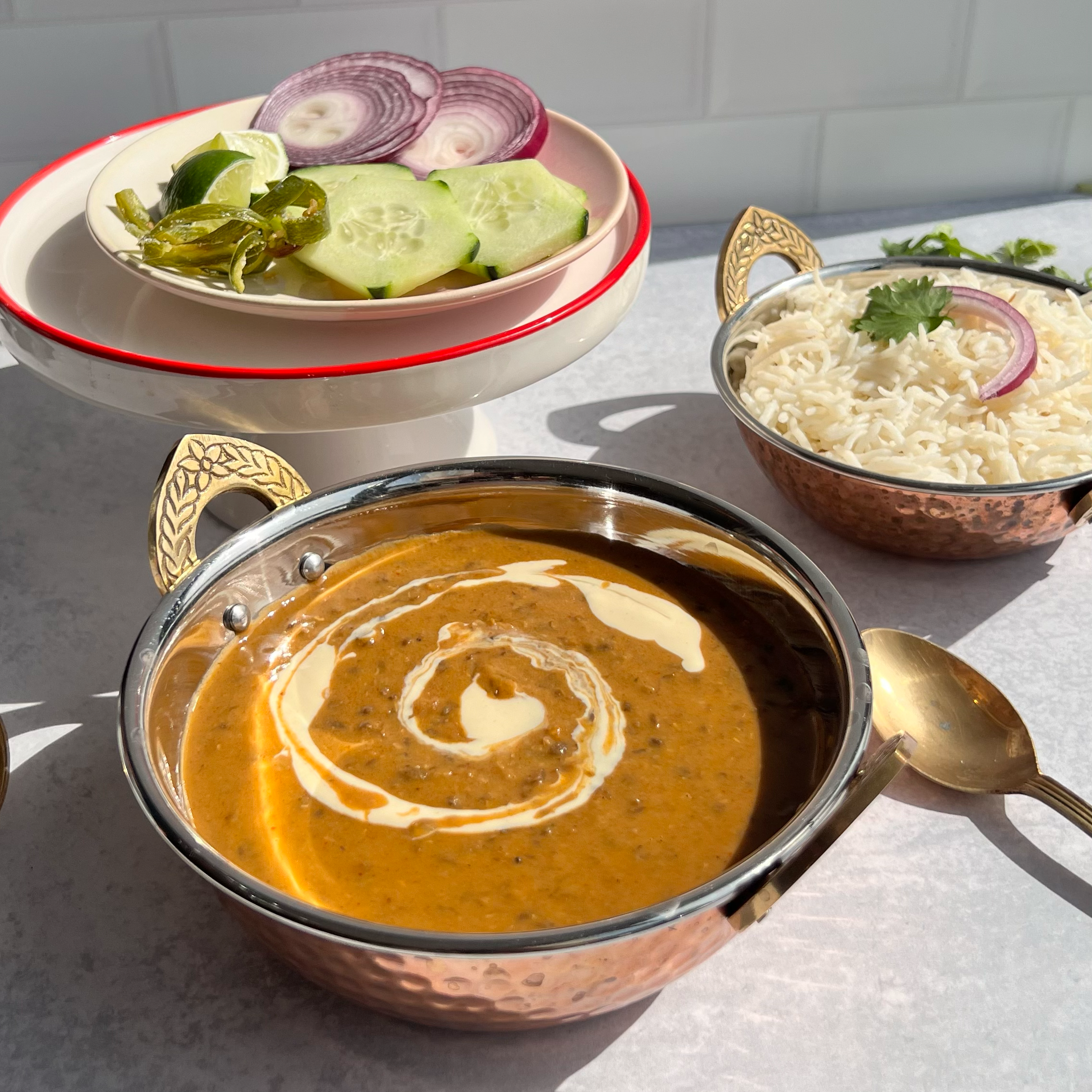 A bowl of Indian lentil soup with a cream swirl, served with rice and a side salad.