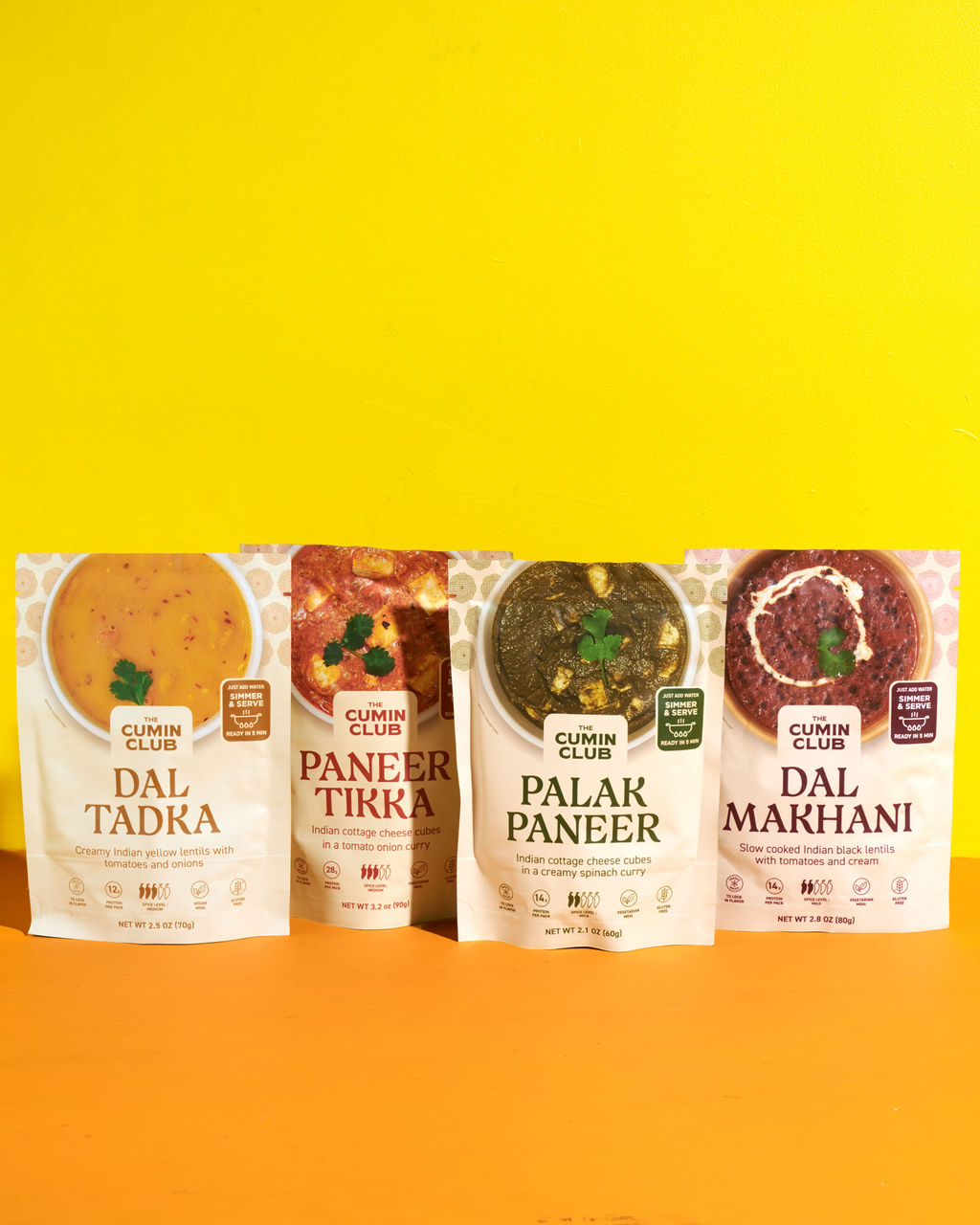 Four packaged Indian meals against a yellow background.