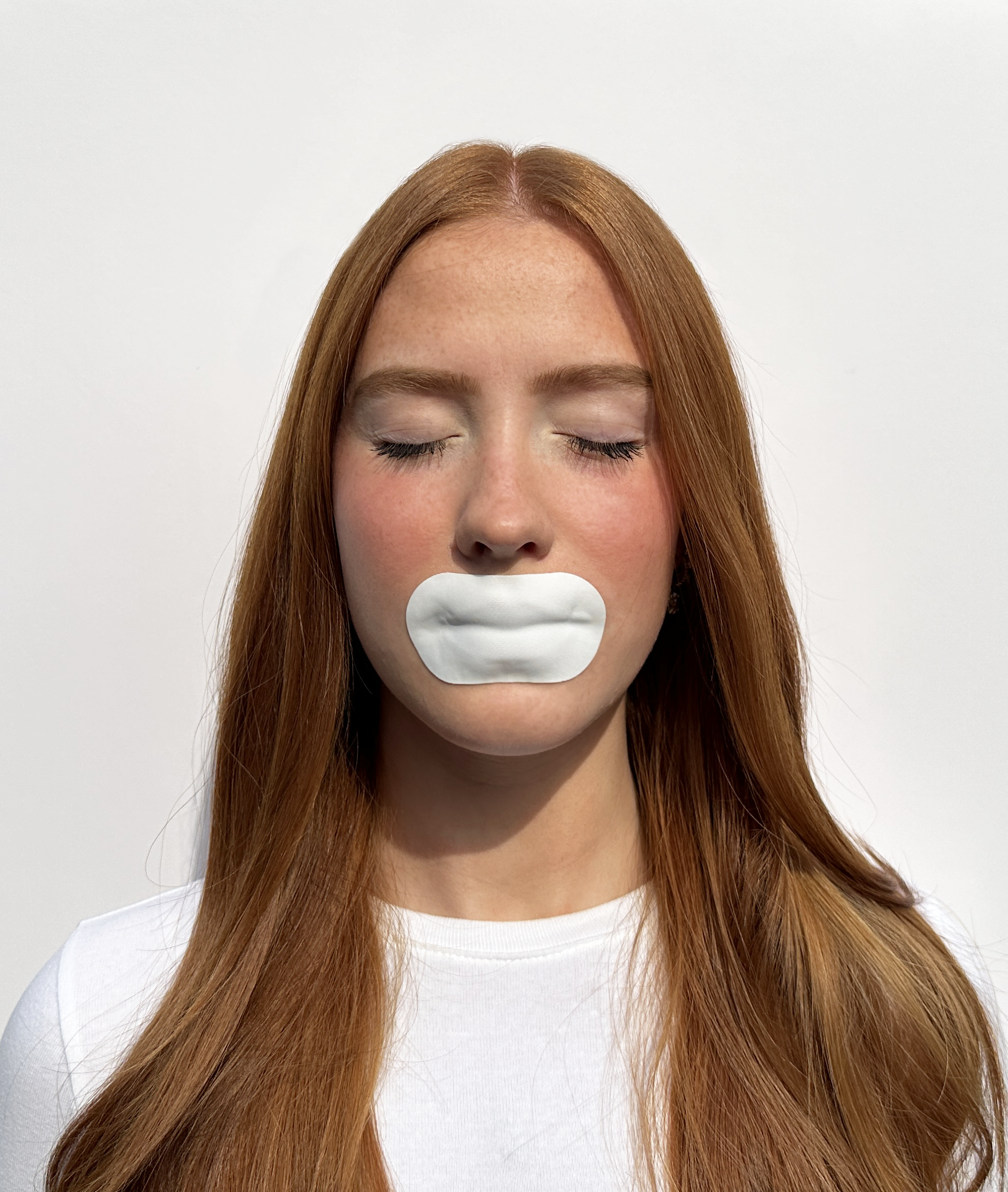 Person with closed eyes and white patch over mouth against plain background.
