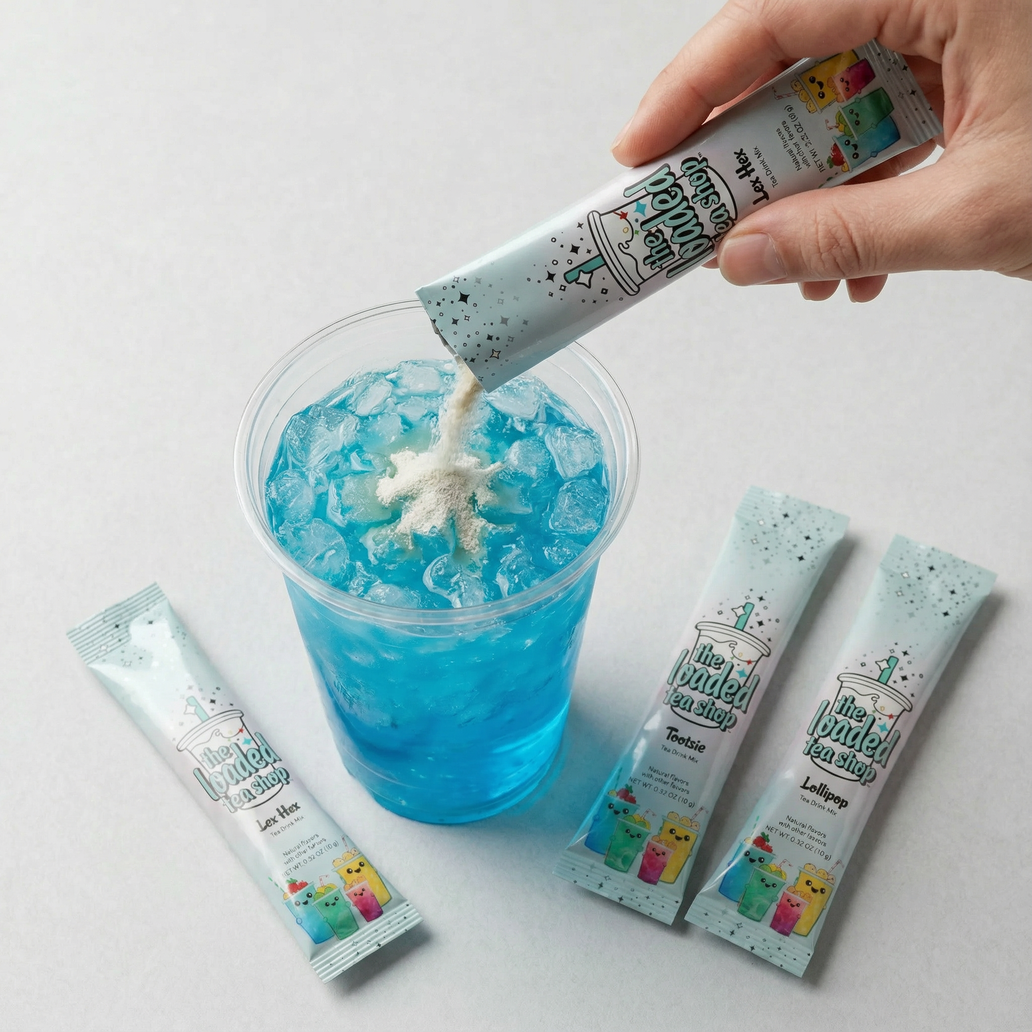 Hand pouring powder into a blue iced drink with three sachets beside.