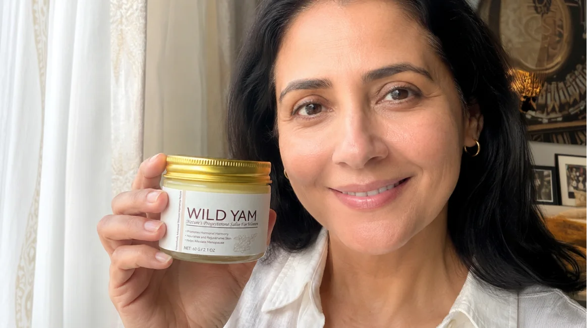 A woman with dark hair smiles while holding up a jar of Wild Yam salve.