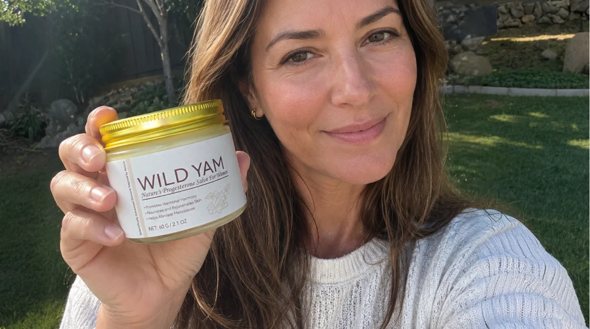 A woman in a white sweater smiles while holding up a jar of Wild Yam progesterone salve.