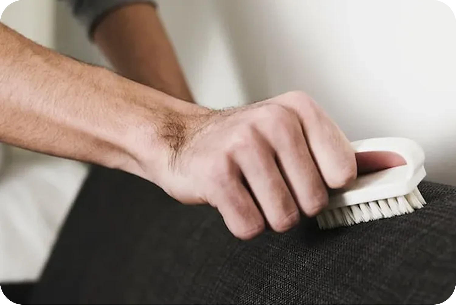 A person uses a white bristle brush to scrub a piece of dark fabric upholstery.