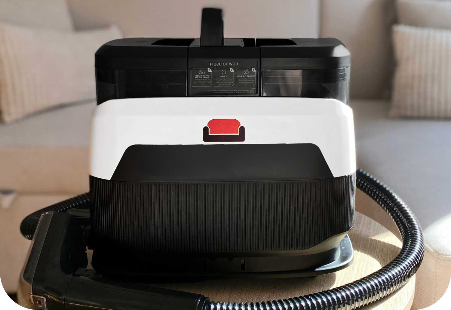 A portable black and white spot cleaner with a hose and nozzle attachment against a white background.